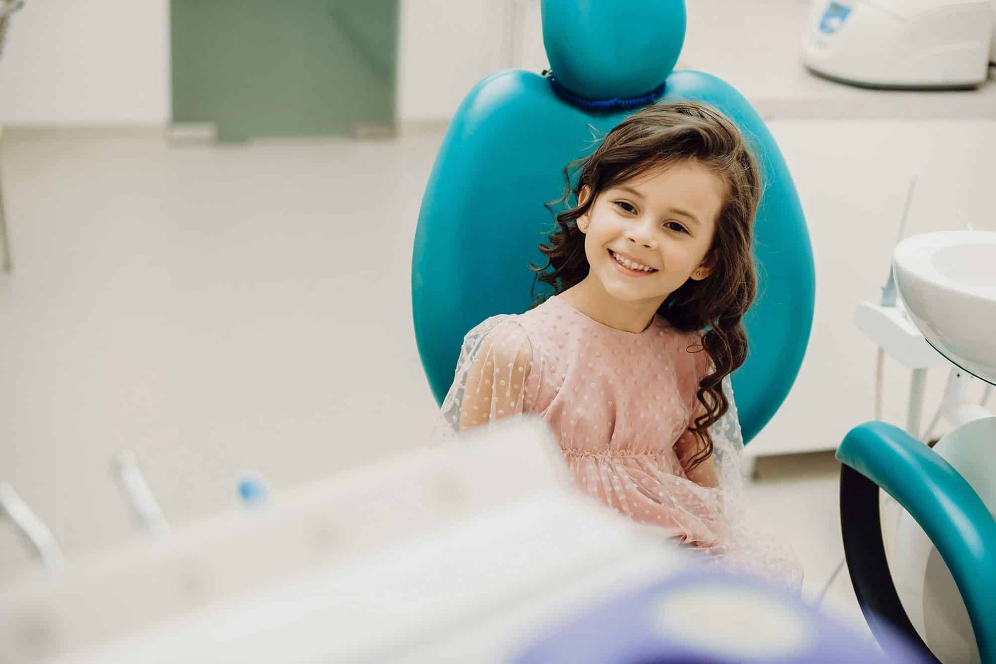 Smiling young girl sitting in a dental chair at the dentist's office.