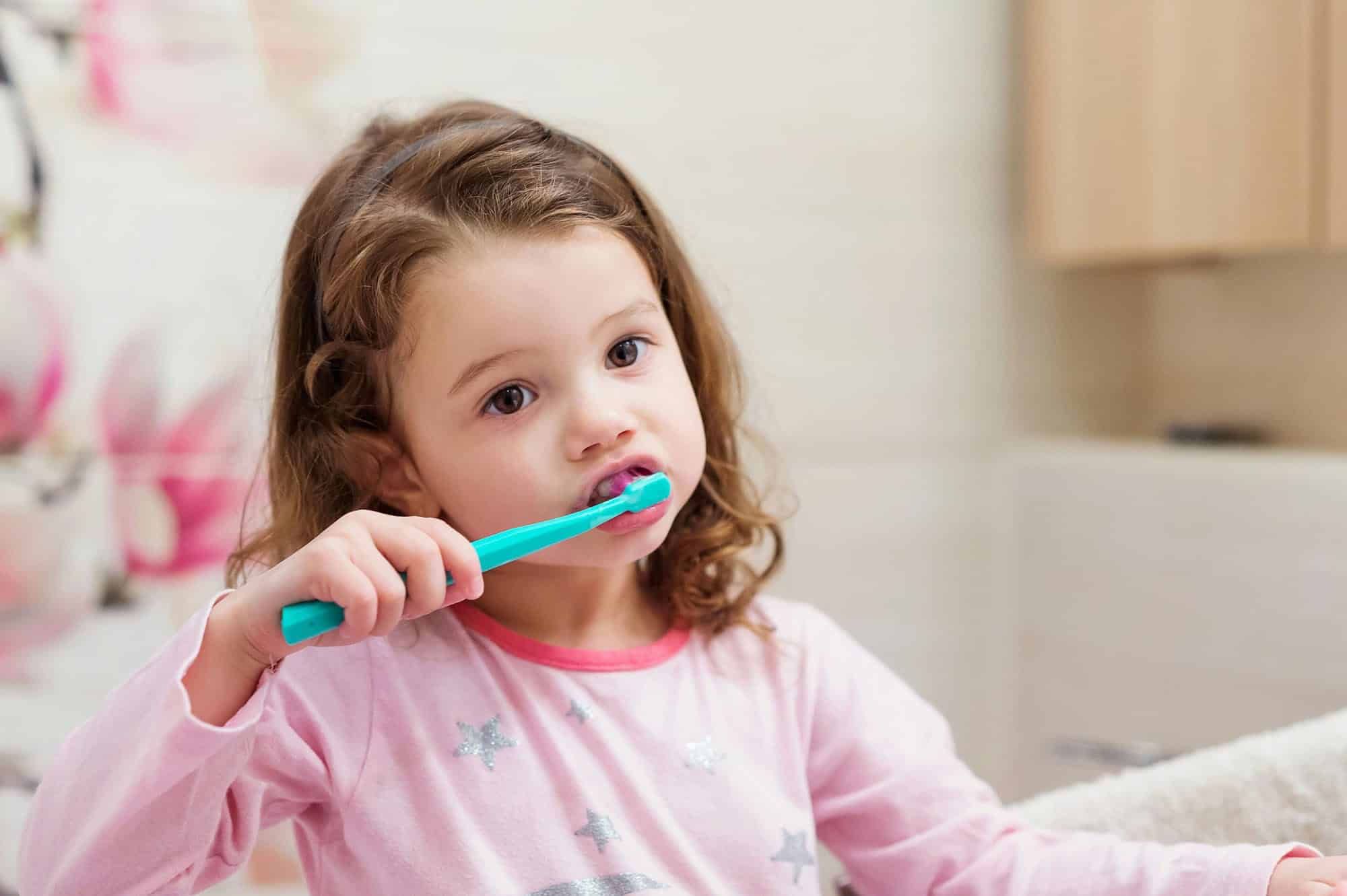 A young girl with brown hair brushing her teeth with a blue toothbrush.