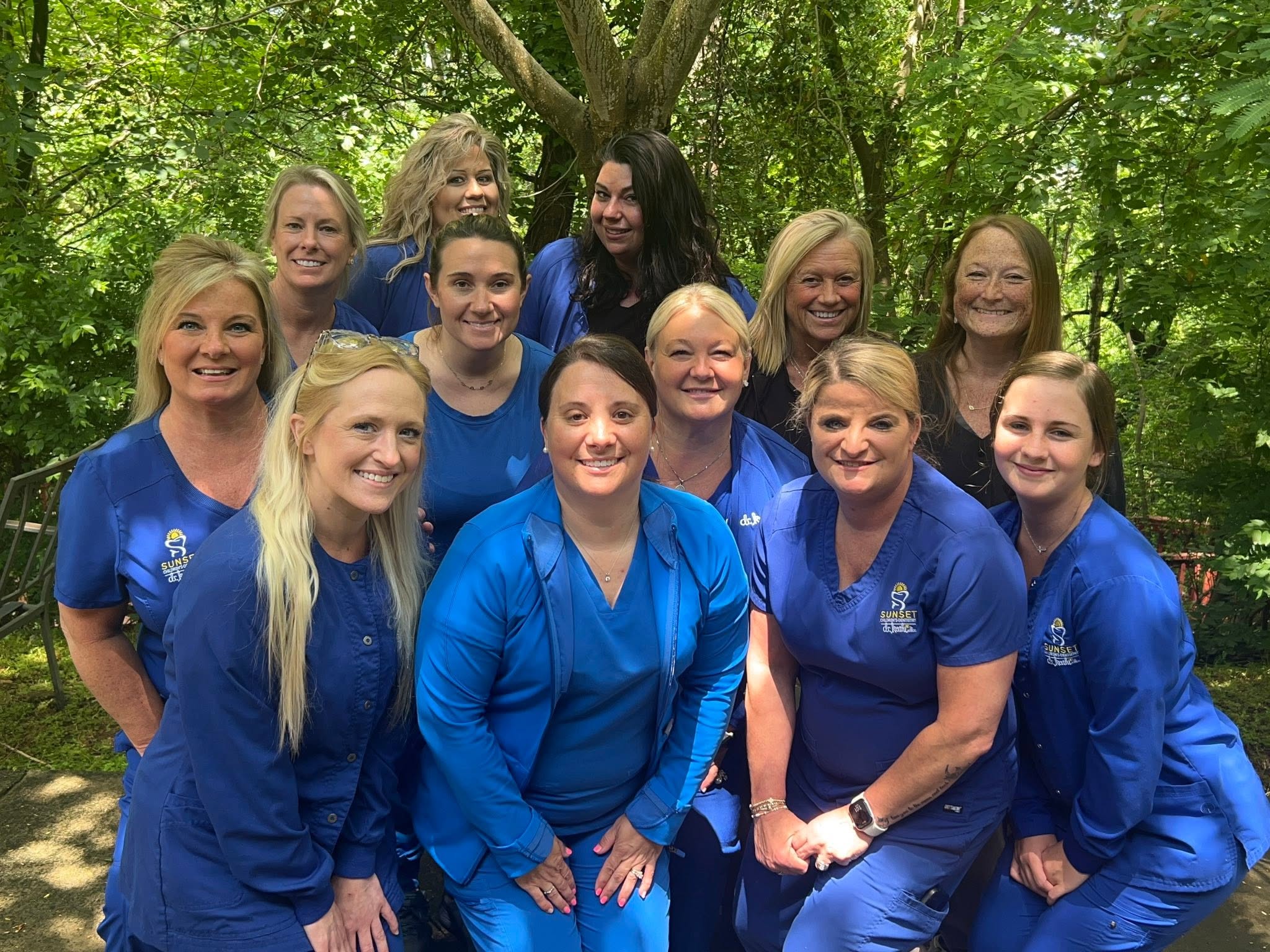 Our kids dental staff wearing blue scrubs posing together outdoors among trees.