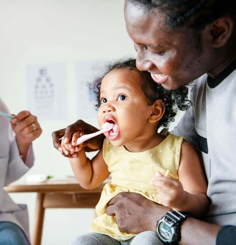 Baby on a parent's lap at a first dental visit, showing when to take baby to dentist